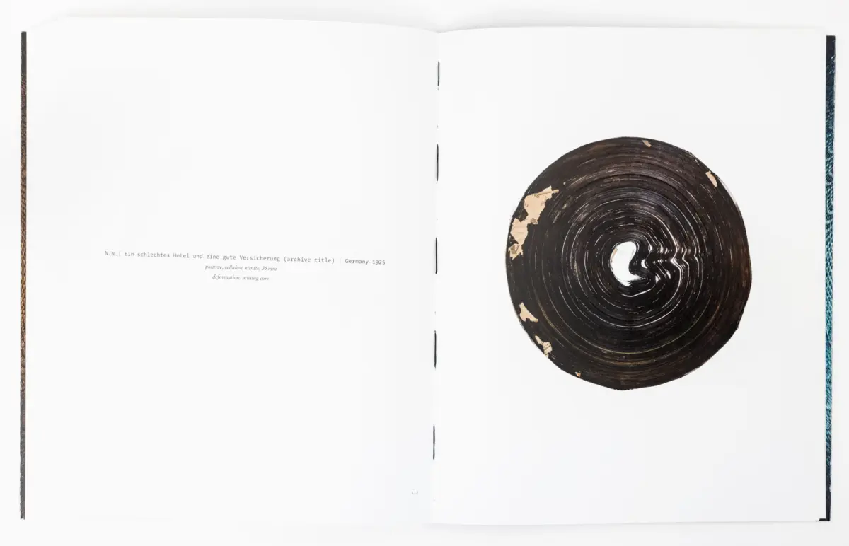 Open book with blank pages; on the right page a large shellac record with visible grooves and peeling edge.