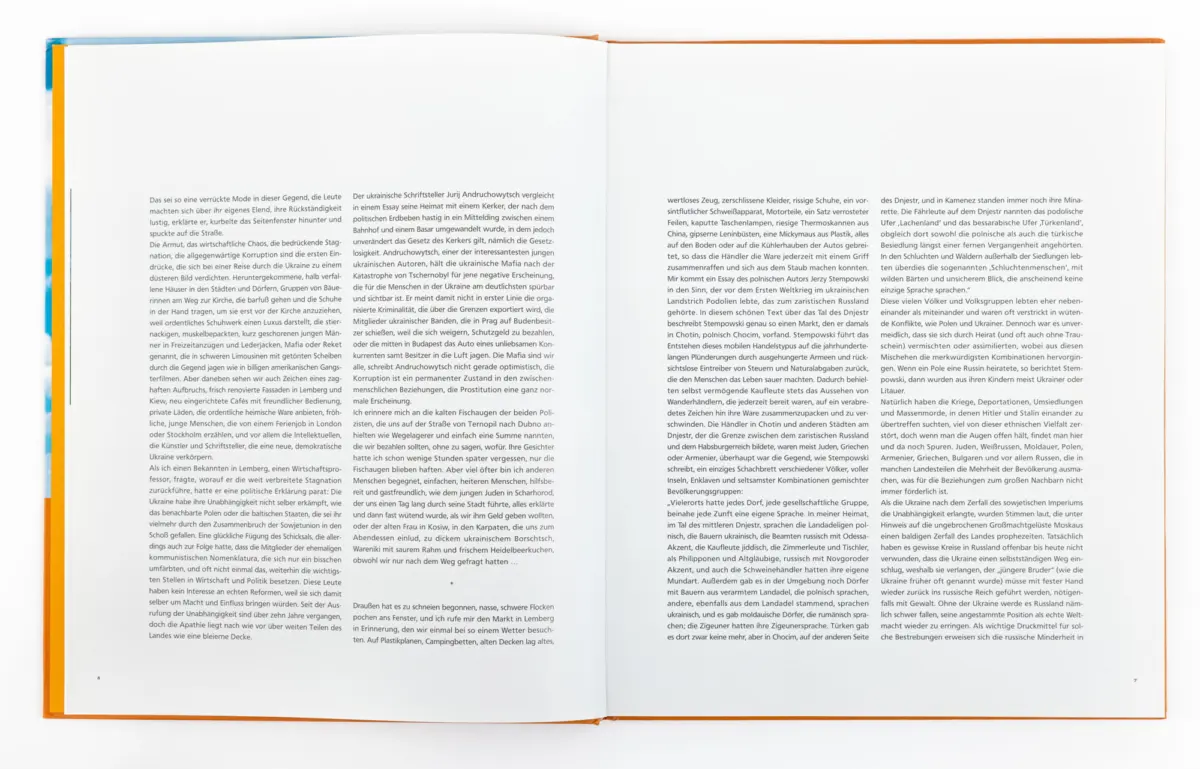 Open two-page book with dense German text on a white surface; orange and blue cover edges visible.