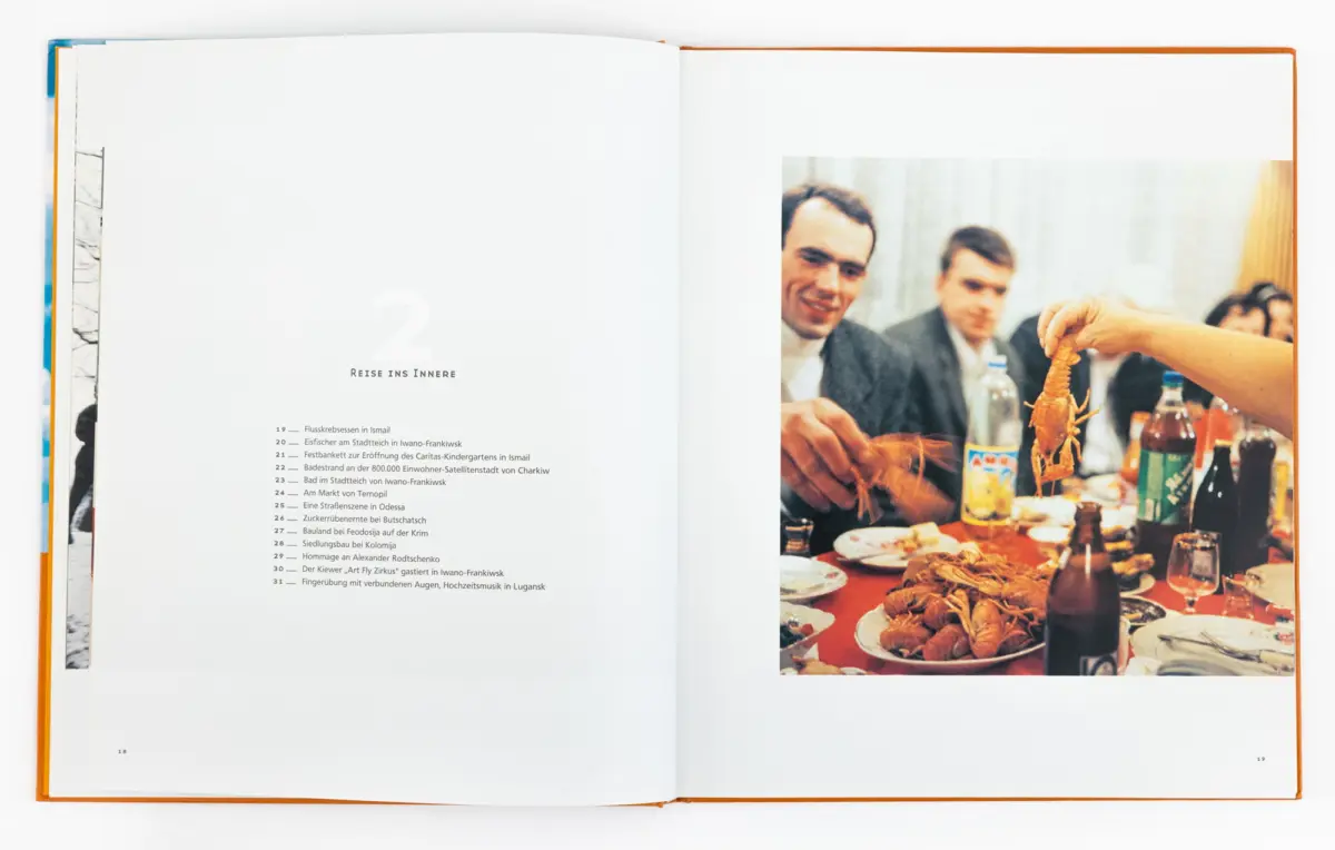Hand raises a lobster at a banquet table; three suited men dine in the background.