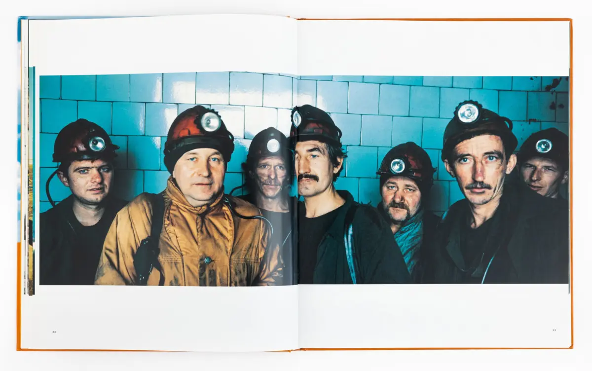 Group of miners wearing helmets with headlamps, posing in front of a blue tiled wall.
