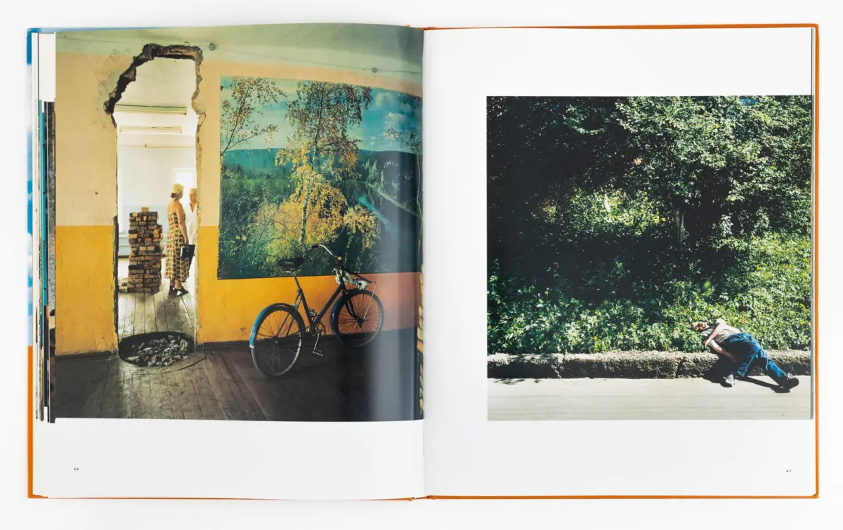 Open book spread: left page shows a yellow interior, bicycle, mural, and two people by a doorway; right page shows dense greenery and a reclining person.