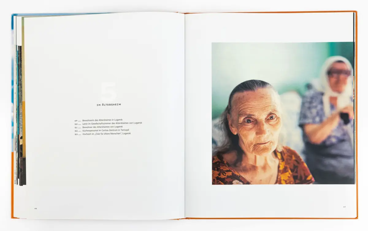 Open book spread; close-up of an elderly woman in a floral dress on the right page, with a blurred man in the background.