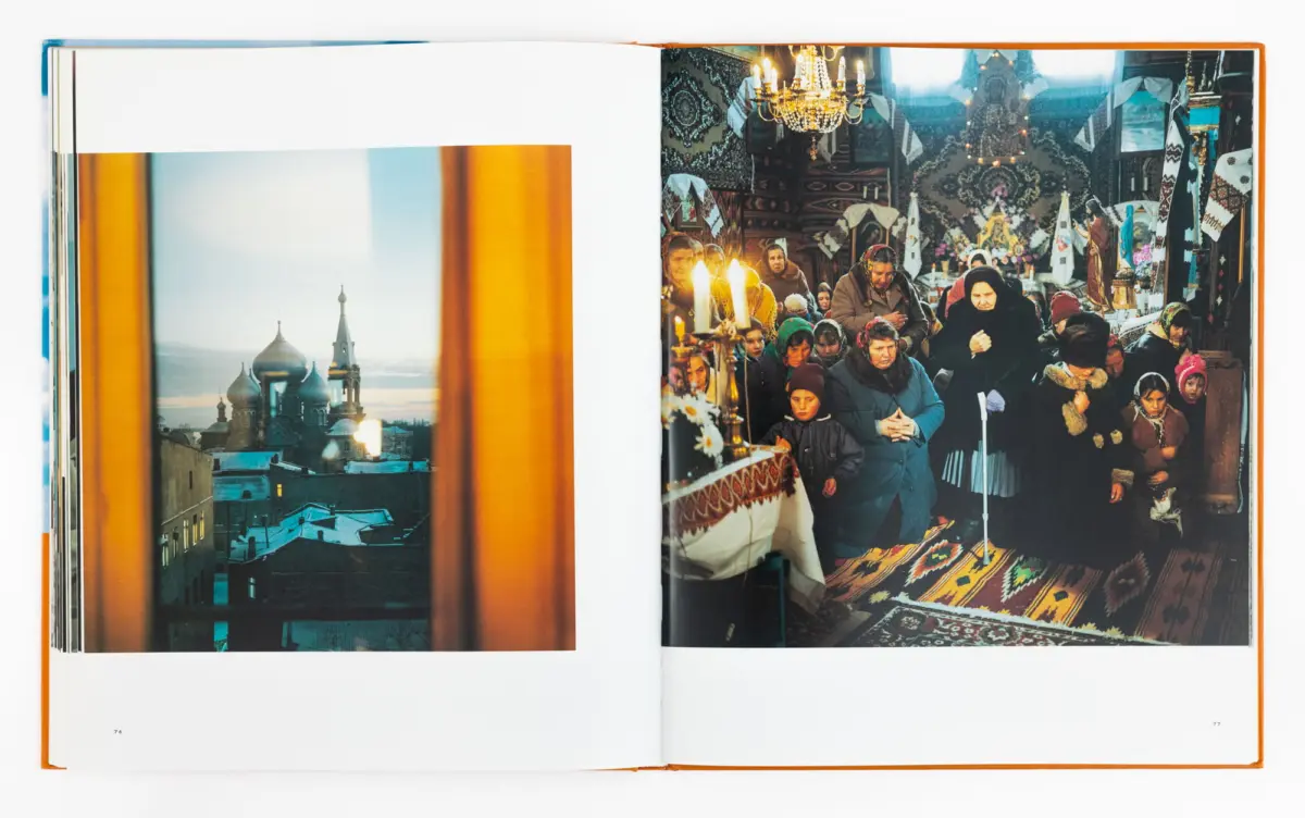 Open photo book spread: left shows snowy city with onion-domed church; right shows crowded church interior with worshippers, candles, chandelier.