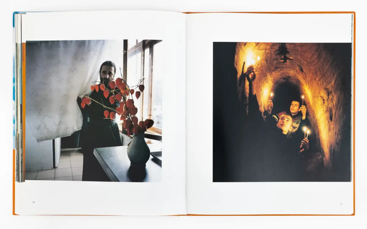 Open book; left: adult man by window with a vase of red-leaf branches; right: people with candles in a dim cave.