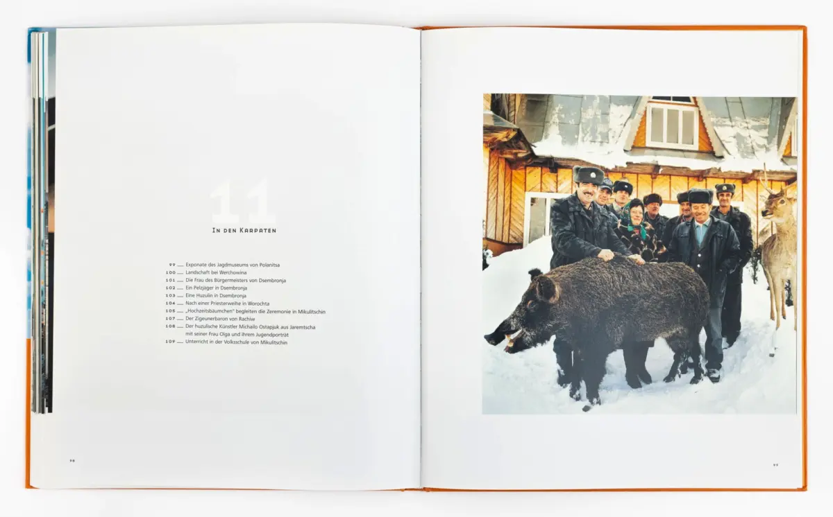 Group of people in fur hats posing with a large bear in a snowy village, wooden houses in the background.