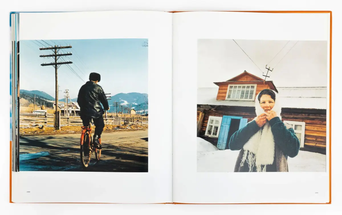 Open book spread: left shows a cyclist on a rural road with utility poles; right shows a woman in a fur hood beside a wooden house in the snow.