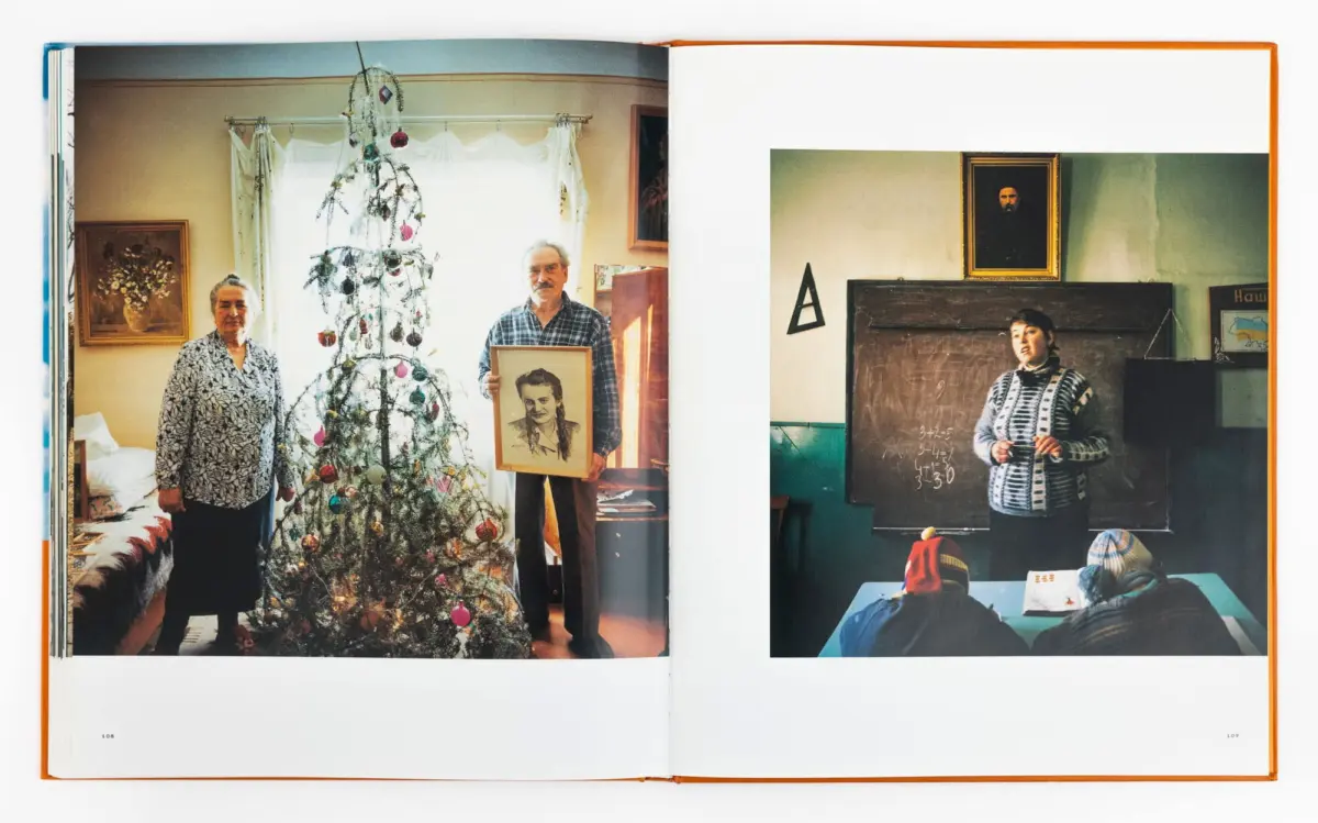 Elderly couple beside a decorated Christmas tree in a living room; man holds a framed portrait. Adjacent scene shows a teacher at a chalkboard.