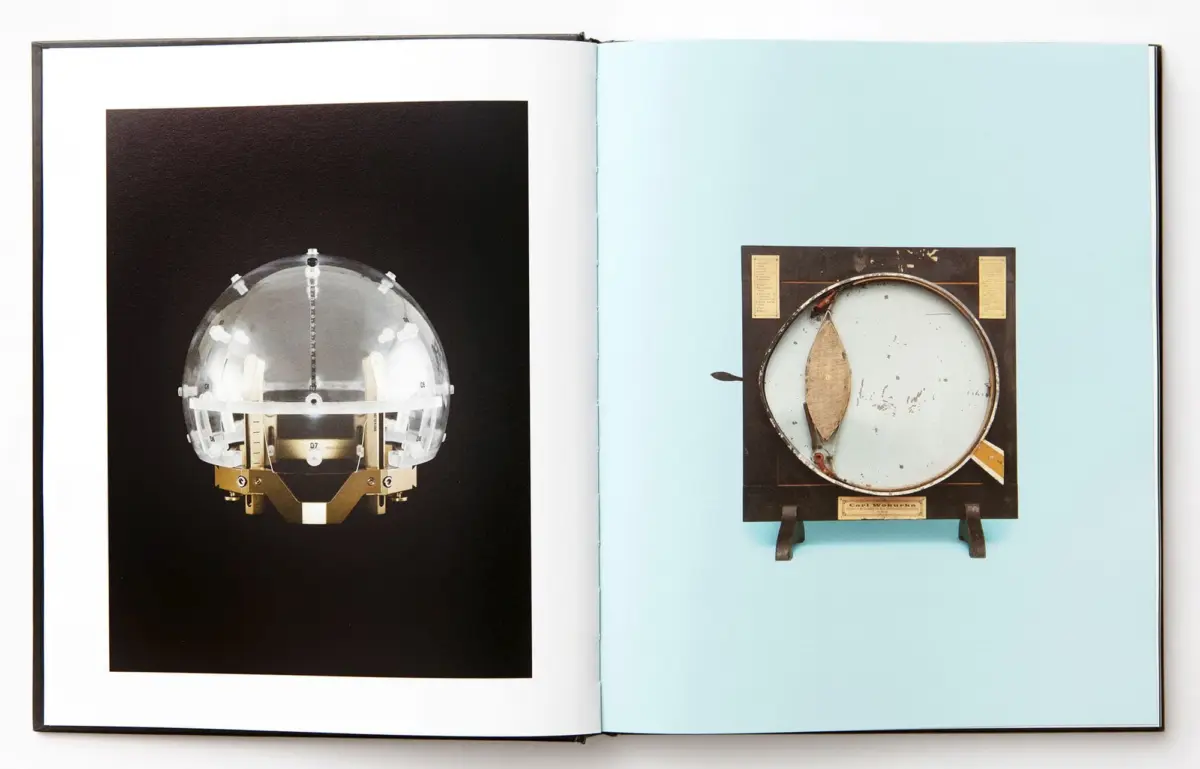 Open book with two images: left a glass hemisphere with metal supports on black; right a circular metal instrument mounted on a wood frame on blue.