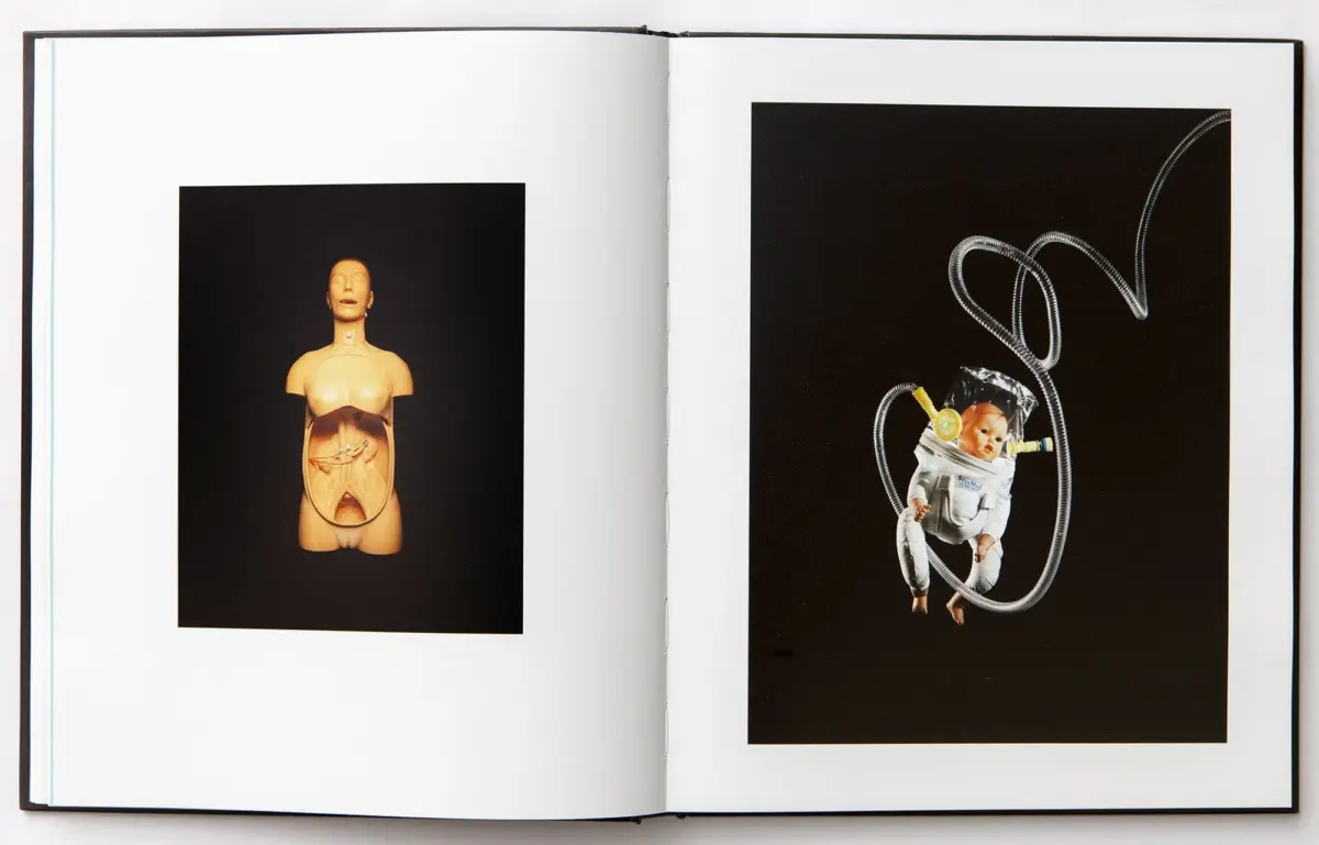 Open book with two images: left a medical mannequin torso exposing internal organs; right a baby in a spacesuit tethered by coiled tubes.