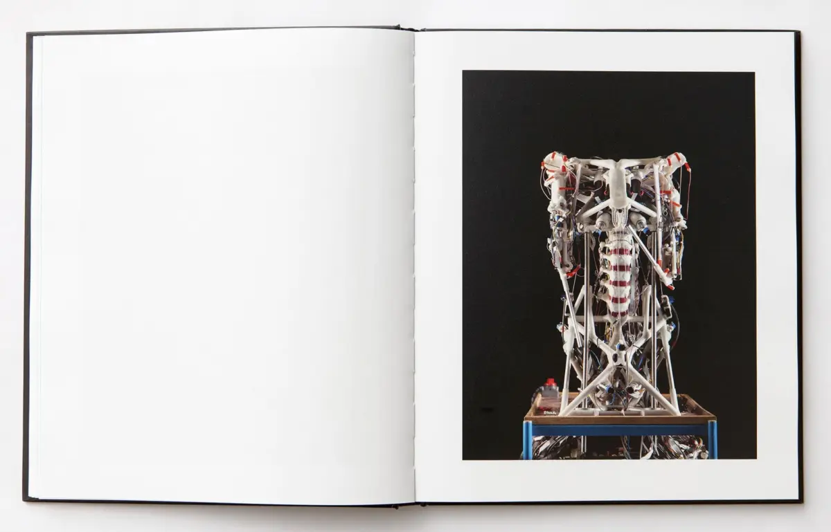 Tall white wire-frame lattice sculpture with red cables on a blue stand against a black backdrop.
