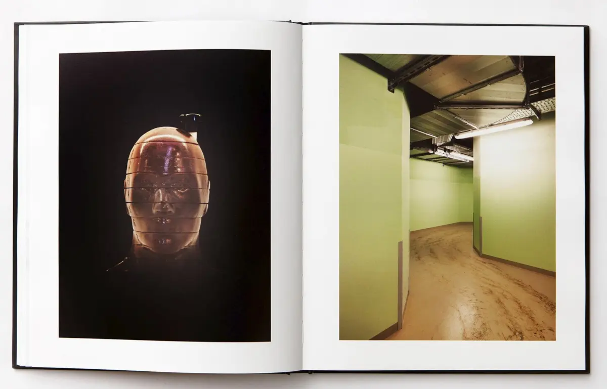 Open book showing left: orange ceramic bust on black; right: lime-green hallway with exposed ducts and fluorescent lights.
