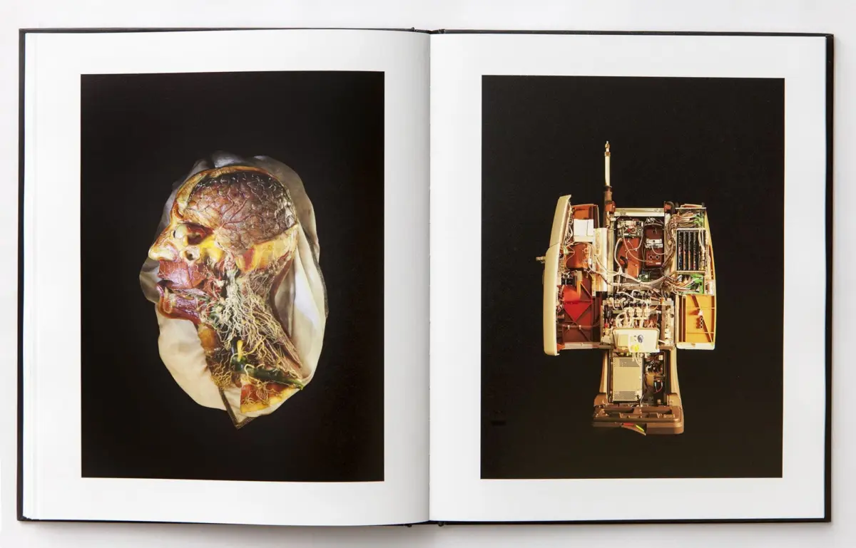 Open book; left page shows a dissected human head cross-section, right page a dismantled electronic device with exposed circuitry.