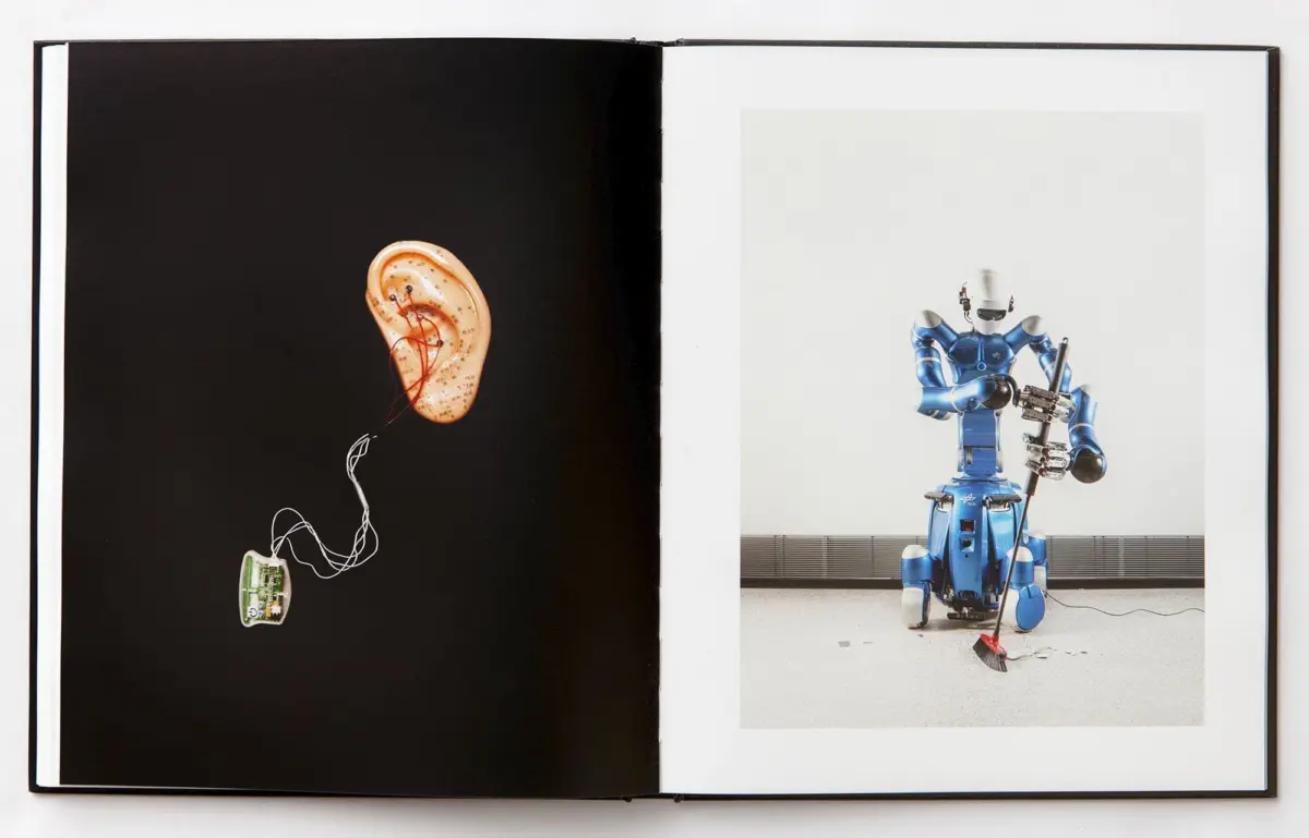 Open book: left page shows an ear connected to a circuit board by wires; right page shows a blue humanoid robot with a guitar-like instrument.