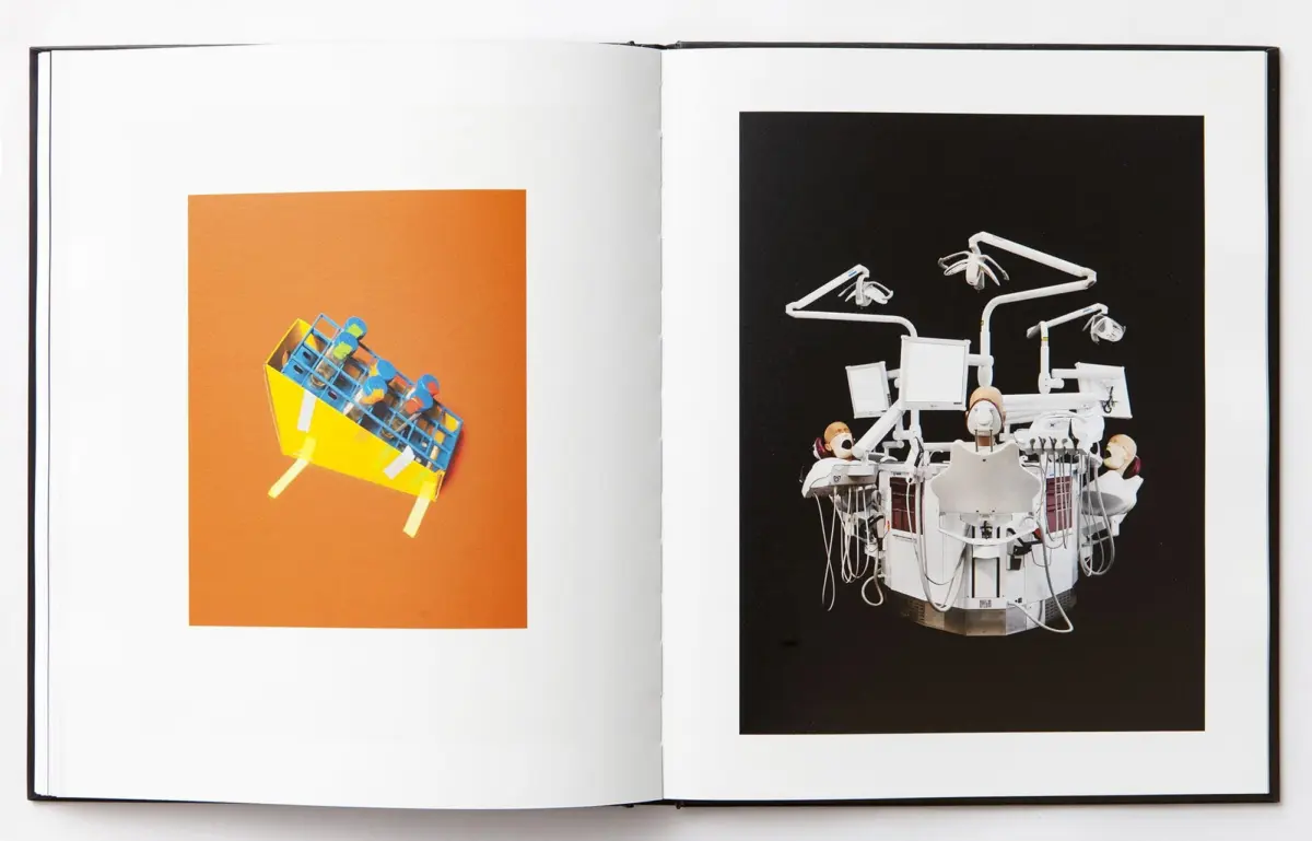 Open book spread: left orange page with a yellow wheeled cart holding blue blocks; right black page with white dental chair equipment.