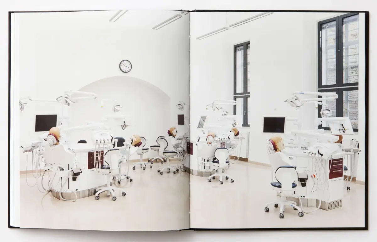 Empty modern dental clinic with several dental chairs and equipment in a bright white room with large windows.