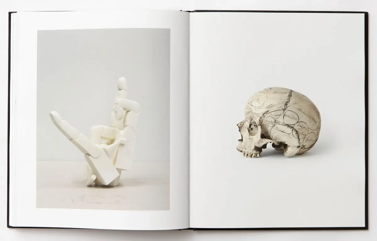 Open book spread: left page shows a white skeletal hand reaching upward; right page shows a skull with engraved map lines.