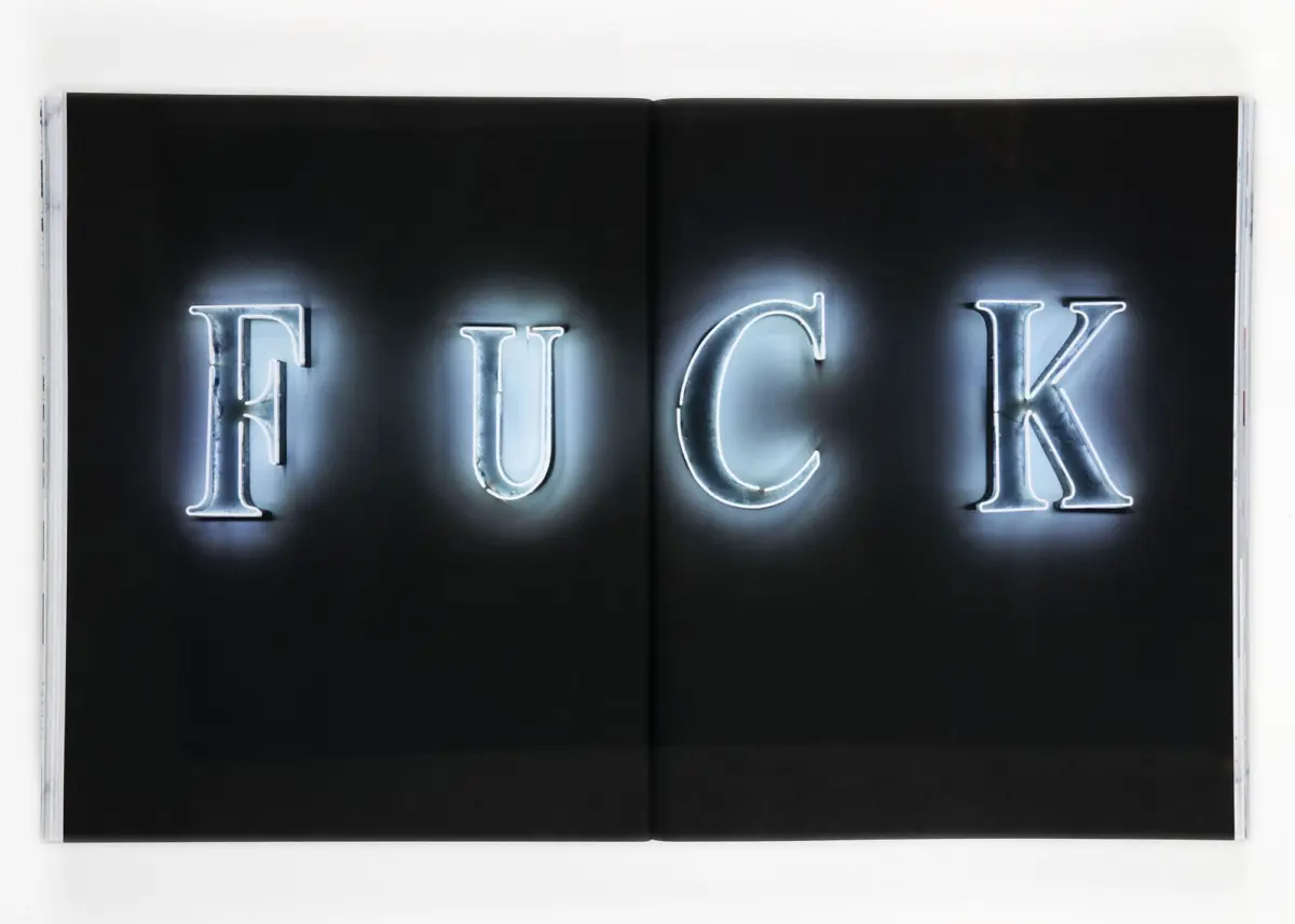 Open two-page book spread displaying glowing neon letters FUCK on a black background
