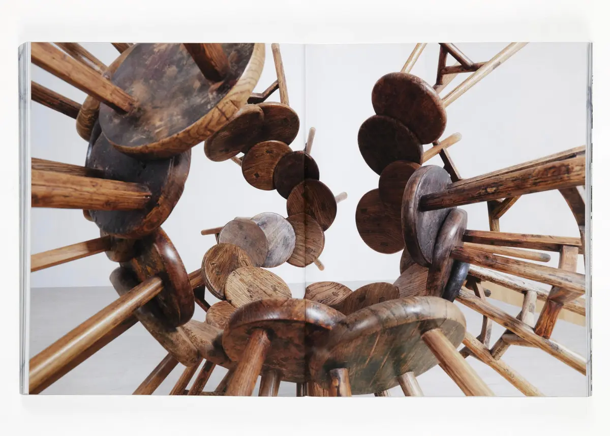 Wooden disc-and-rod sculpture forming a circular tunnel in a white gallery.