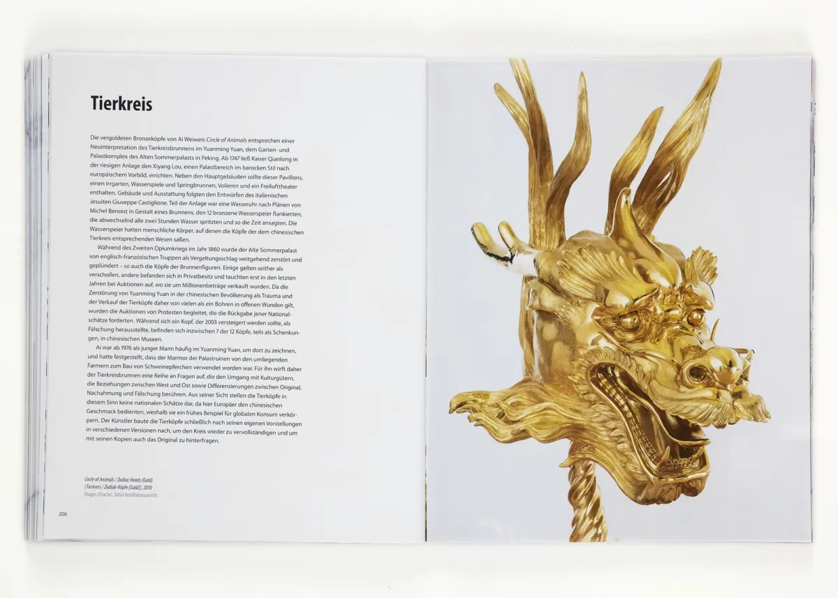 Golden dragon head sculpture on an open book; left page shows German text with the heading Tierkreis.