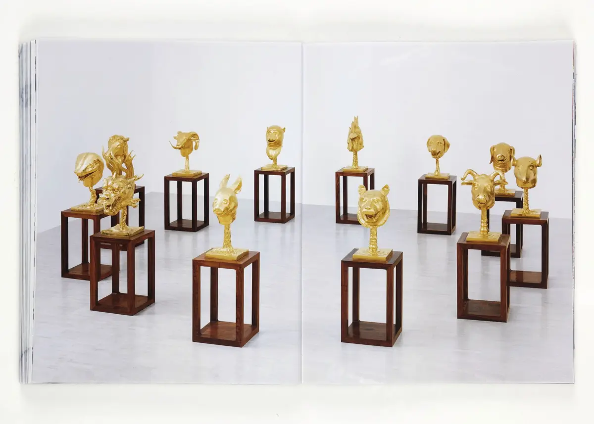 Gold-colored animal head sculptures displayed on wooden pedestals in a white gallery.