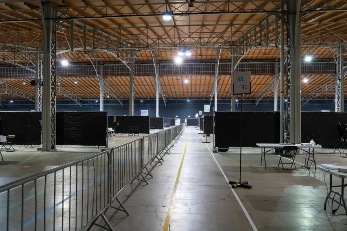 Interior of a large exhibition hall with metal truss framework, black booth panels, and empty rows.