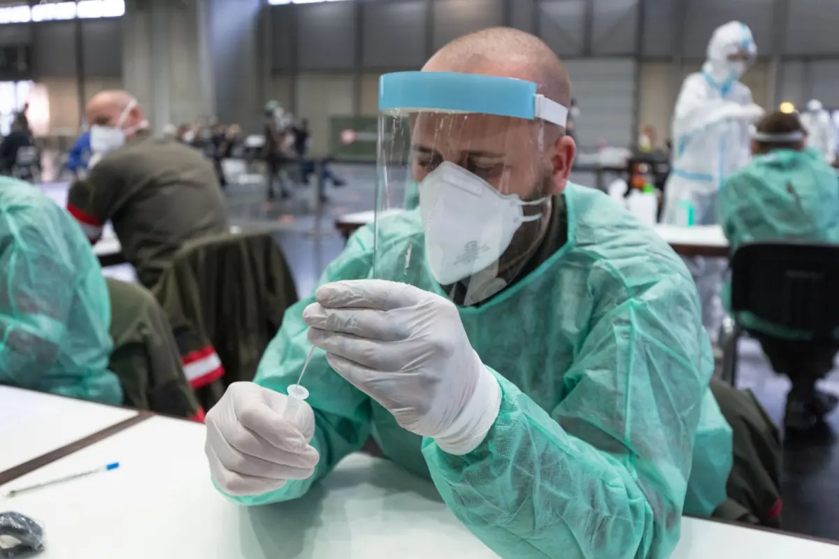 Healthcare worker in PPE with face shield and mask prepares syringe at a vaccination center.