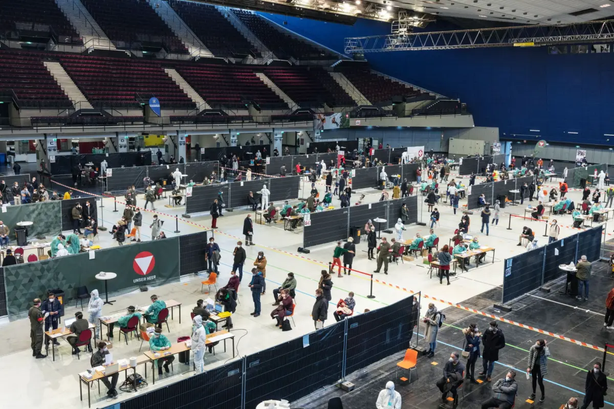 Large indoor arena converted into a vaccination center with multiple booths and people waiting.