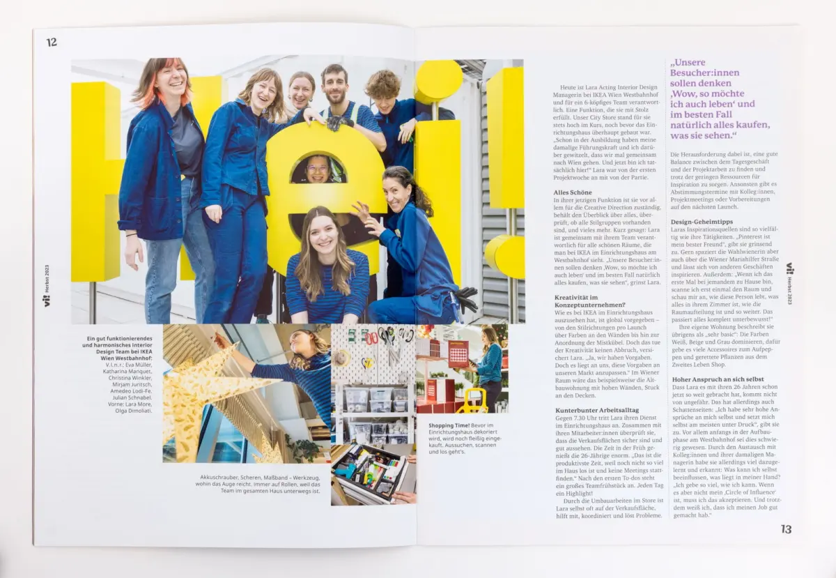 Group of designers in blue outfits posing with oversized yellow letters in a bright studio.