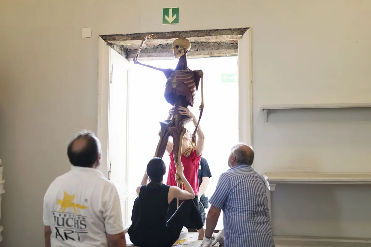Group of people moves a life-size human skeleton prop through a doorway in an art studio.