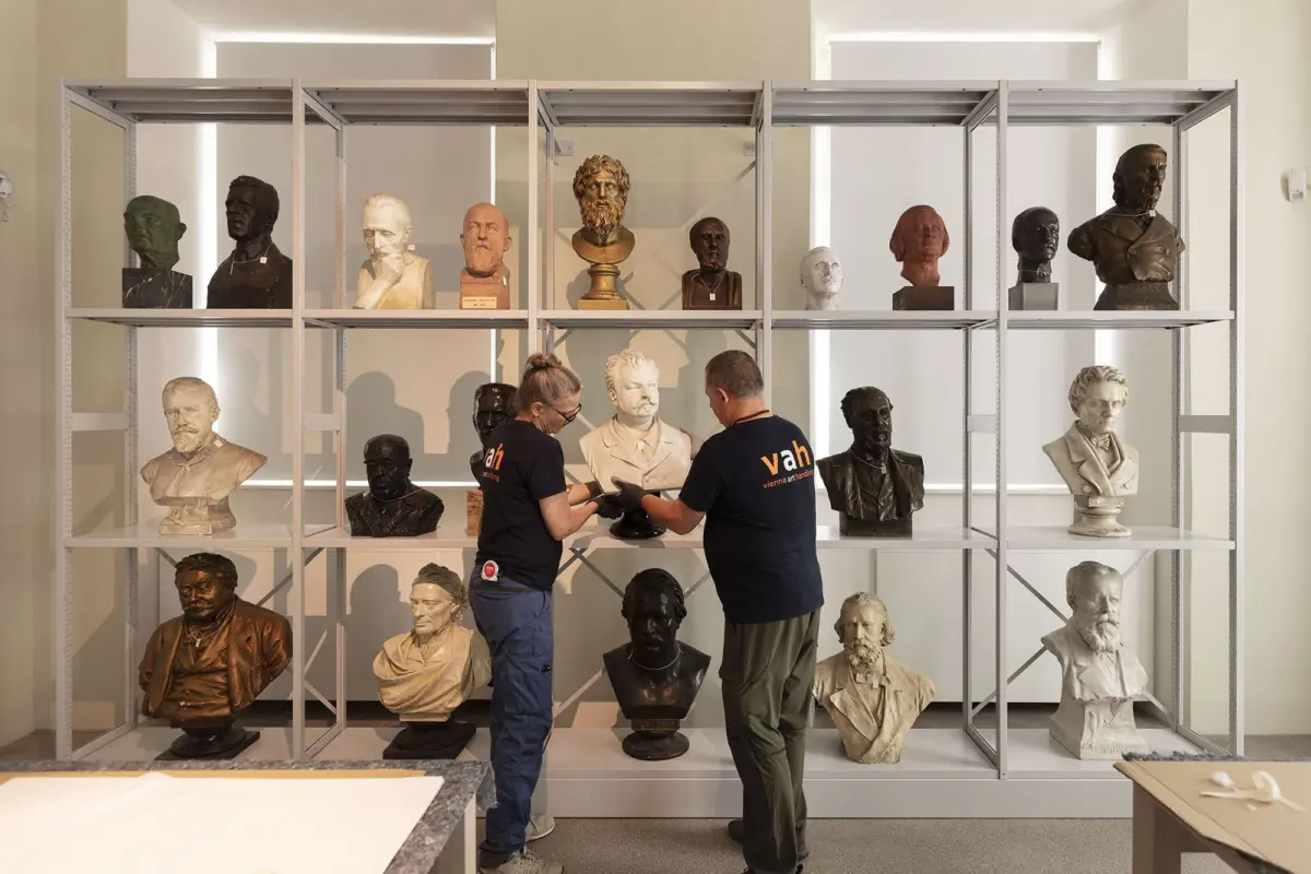 Two conservators handle a bust on a shelf in a sculpture storage room.