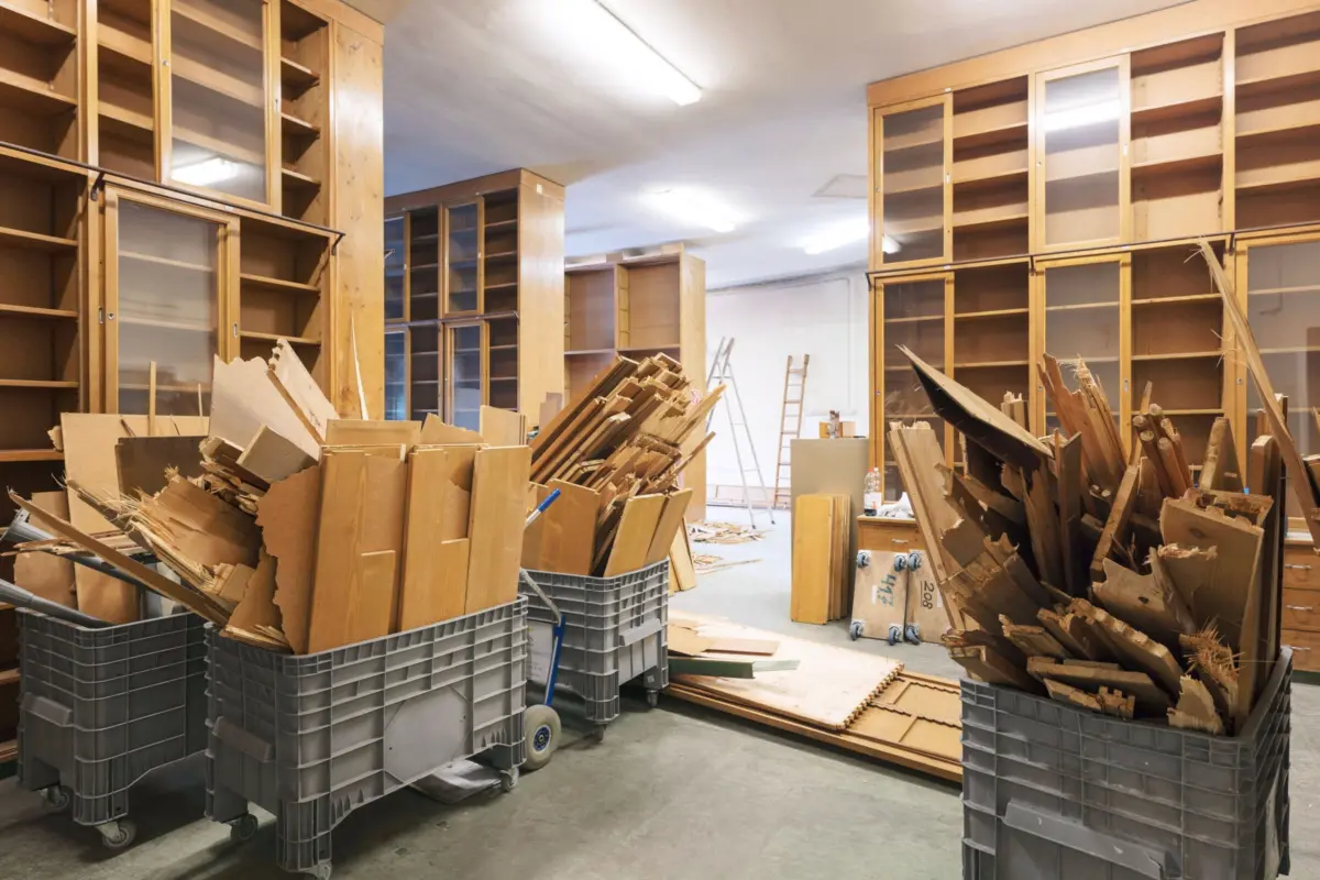Woodworking shop with tall wooden cabinets and glass doors, and large wheeled bins filled with wood scraps.