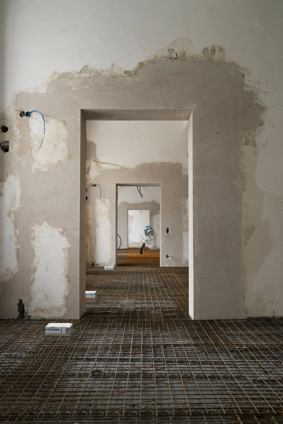 Unfinished interior with receding doorways, rough concrete walls, and a steel rebar floor; blue electrical cables hanging from the walls.