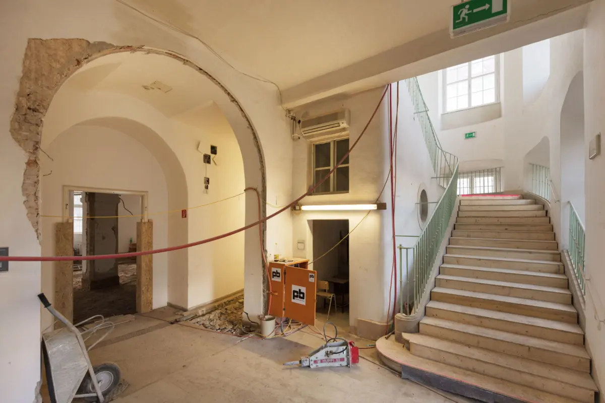 Interior of a historic building under renovation; exposed brick arch, debris, and a stairwell with green railing.