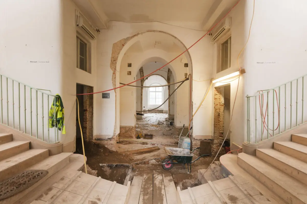 Interior renovation of a building with an arched corridor, exposed brick, debris, and a wheelbarrow.