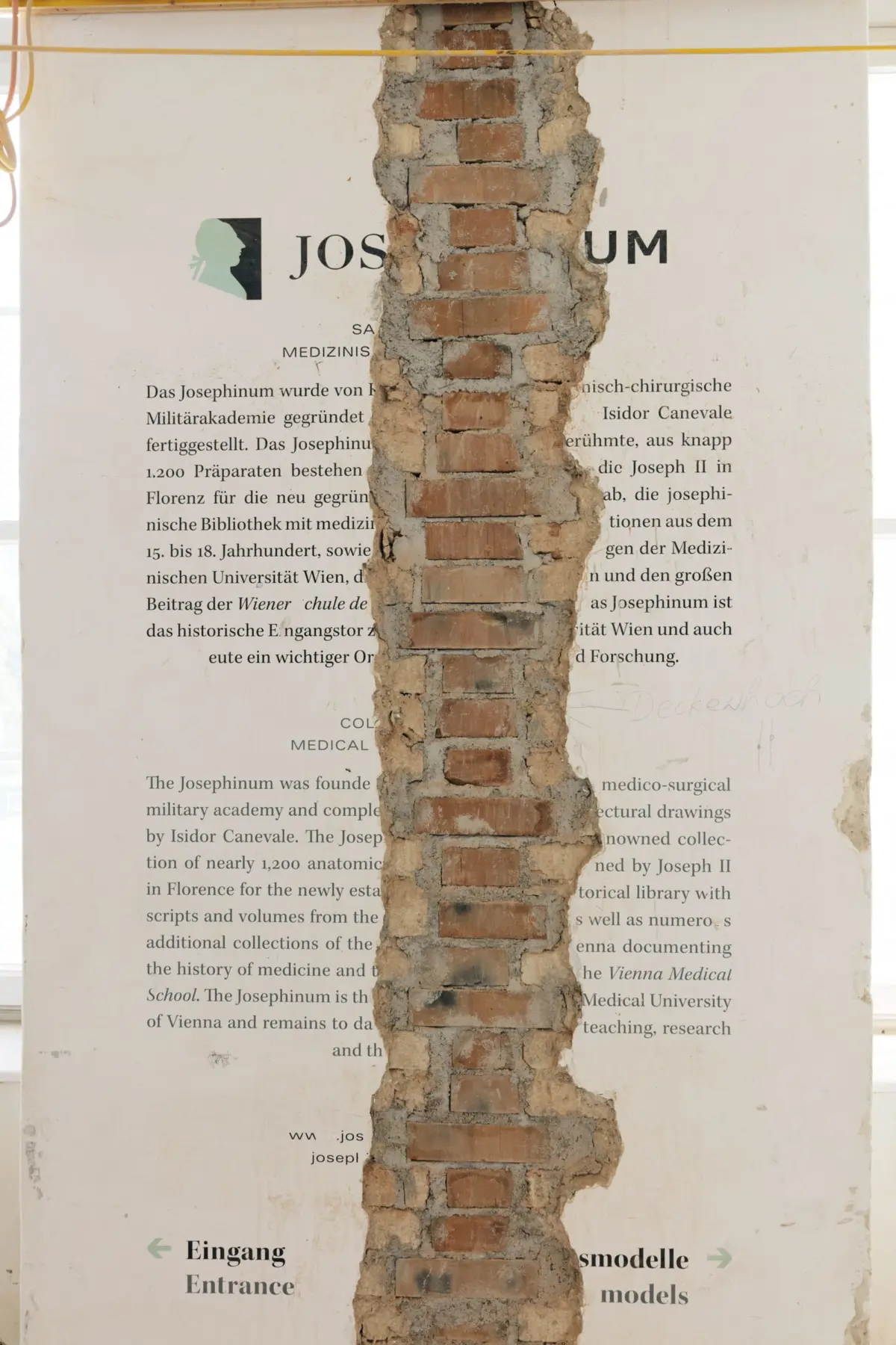 Brick column torn through a white wall poster about the Josephinum, exposing red bricks behind.