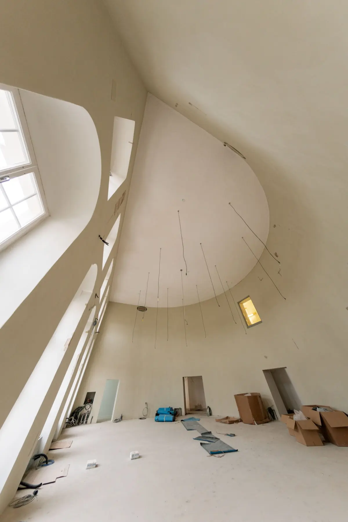 Interior of a tall, curved-walled room under renovation; hanging wires from the ceiling, scattered boxes and construction materials.