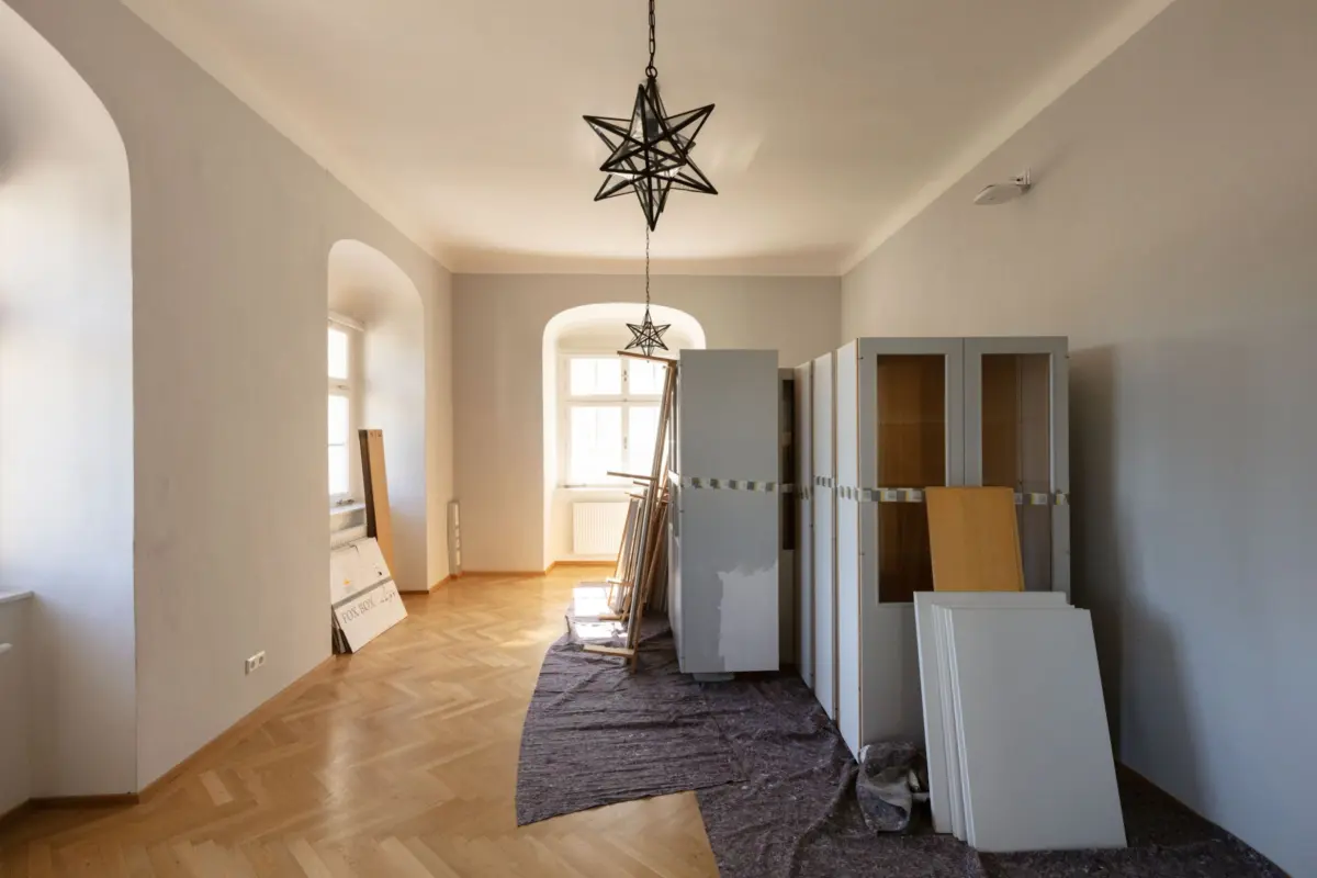 Interior under renovation with two geometric star pendant lights, gray walls, and herringbone hardwood floor; cabinets and wood panels stacked on the right.