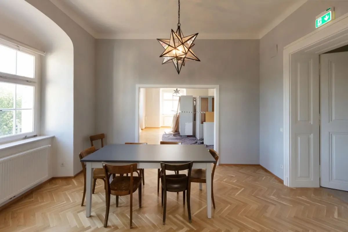 Star-shaped geometric pendant light hangs over a gray dining table with wooden chairs; adjacent room shows construction.