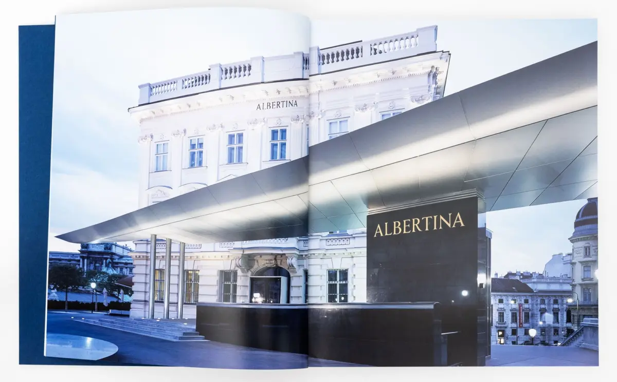Albertina museum with ornate classical facade and balconies, viewed behind a modern metallic canopy.