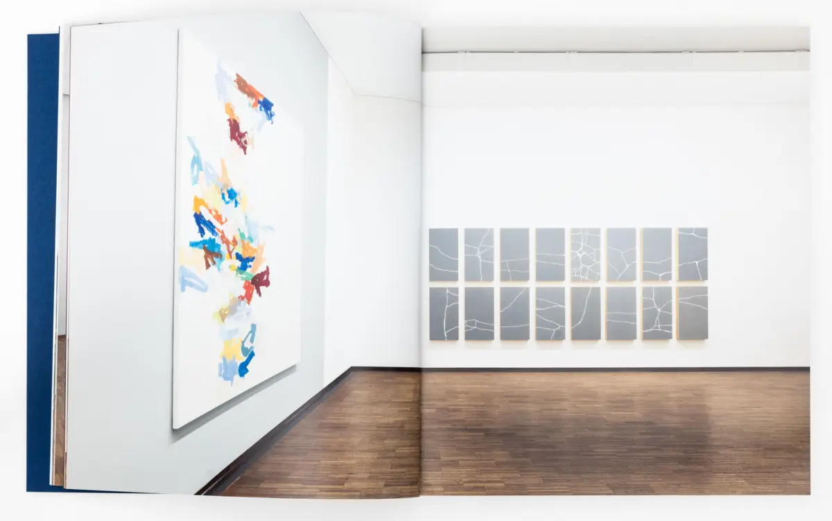 Modern art gallery interior with a large colorful abstract painting on the left and a grid of gray crackle-textured tiles on the right.
