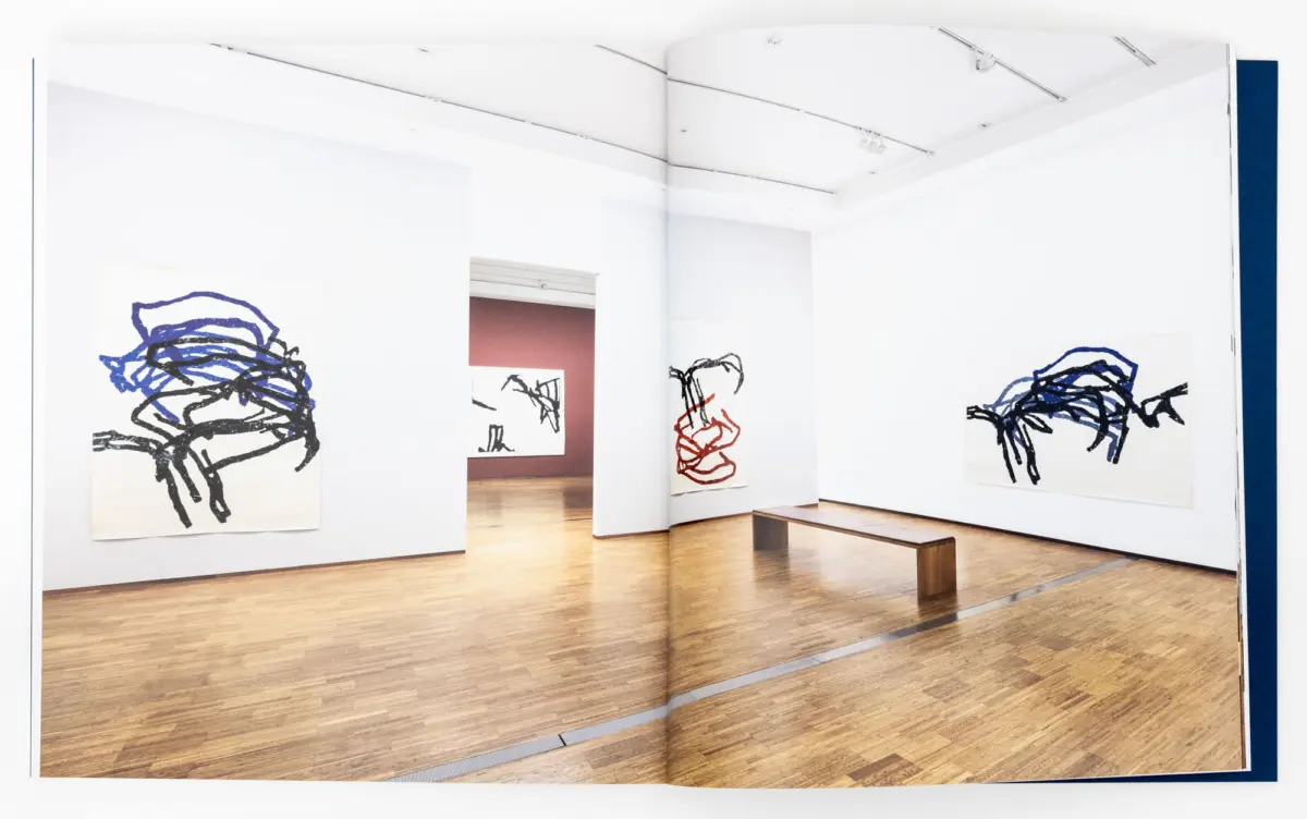 Abstract ink drawings on large white sheets hung on bright white gallery walls; wooden floor and a bench in the foreground.