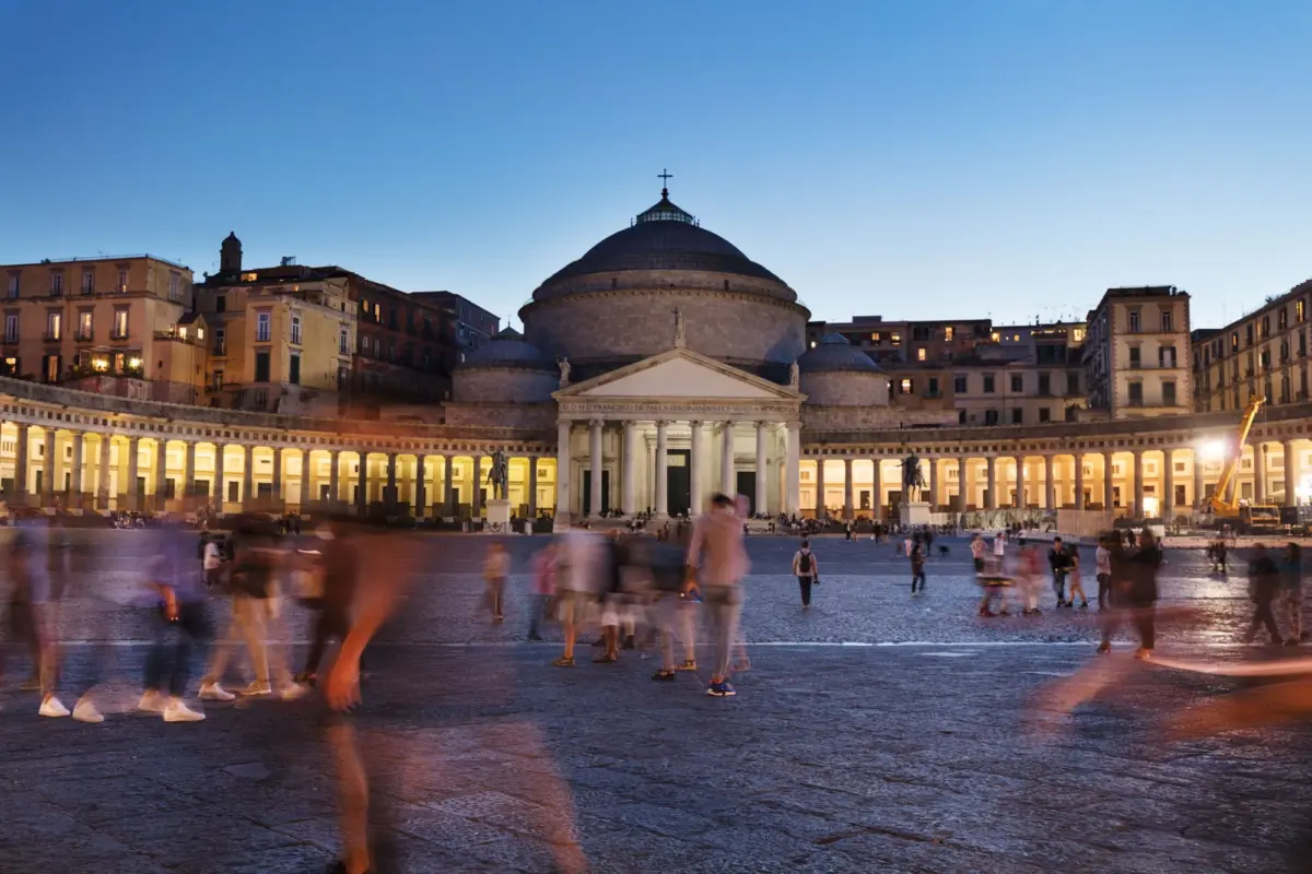 Domed neoclassical church San Francesco diPaola in Piazza del Plebiscito, Naples, at dusk; blurred pedestrians in foreground.