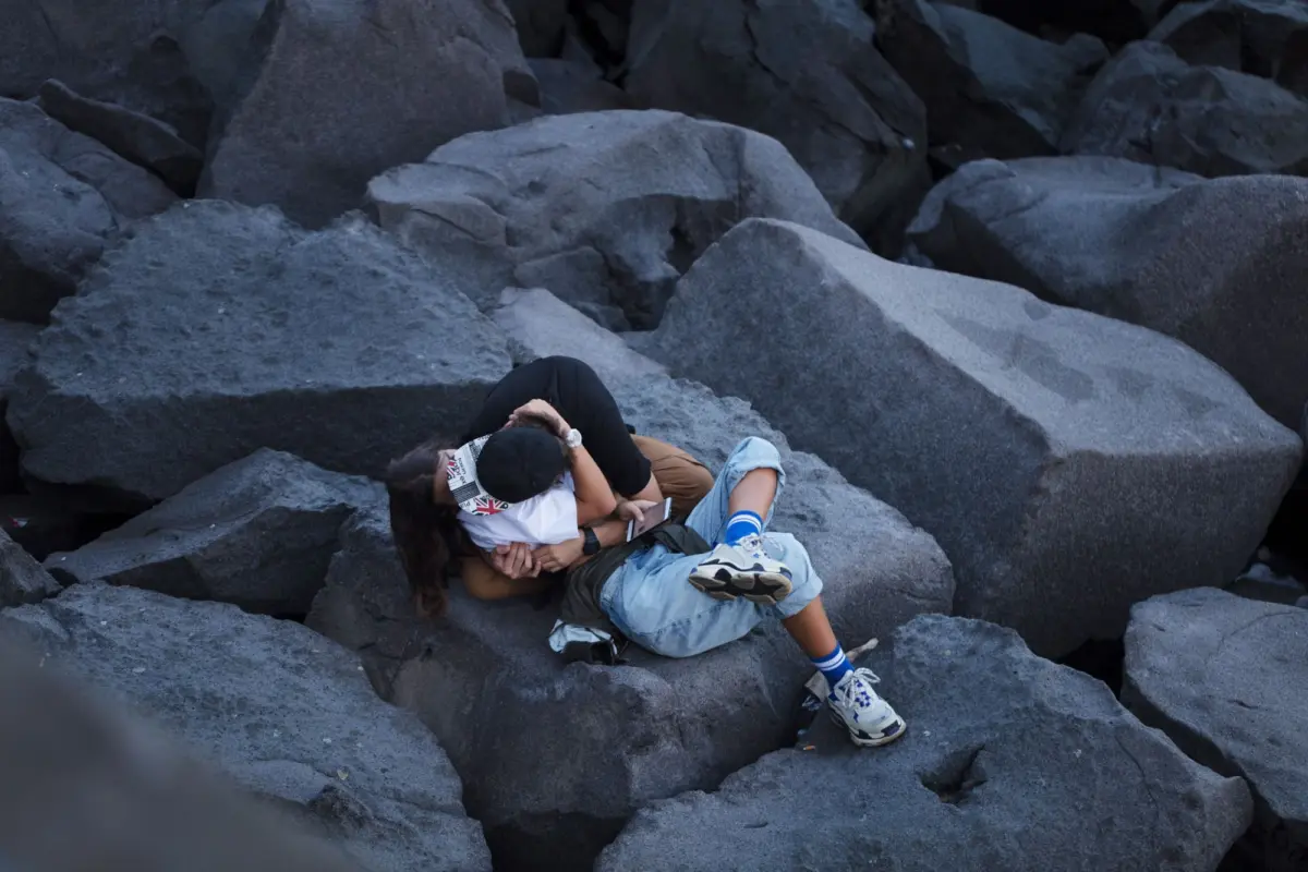 Two people embracing on large gray volcanic rocks.