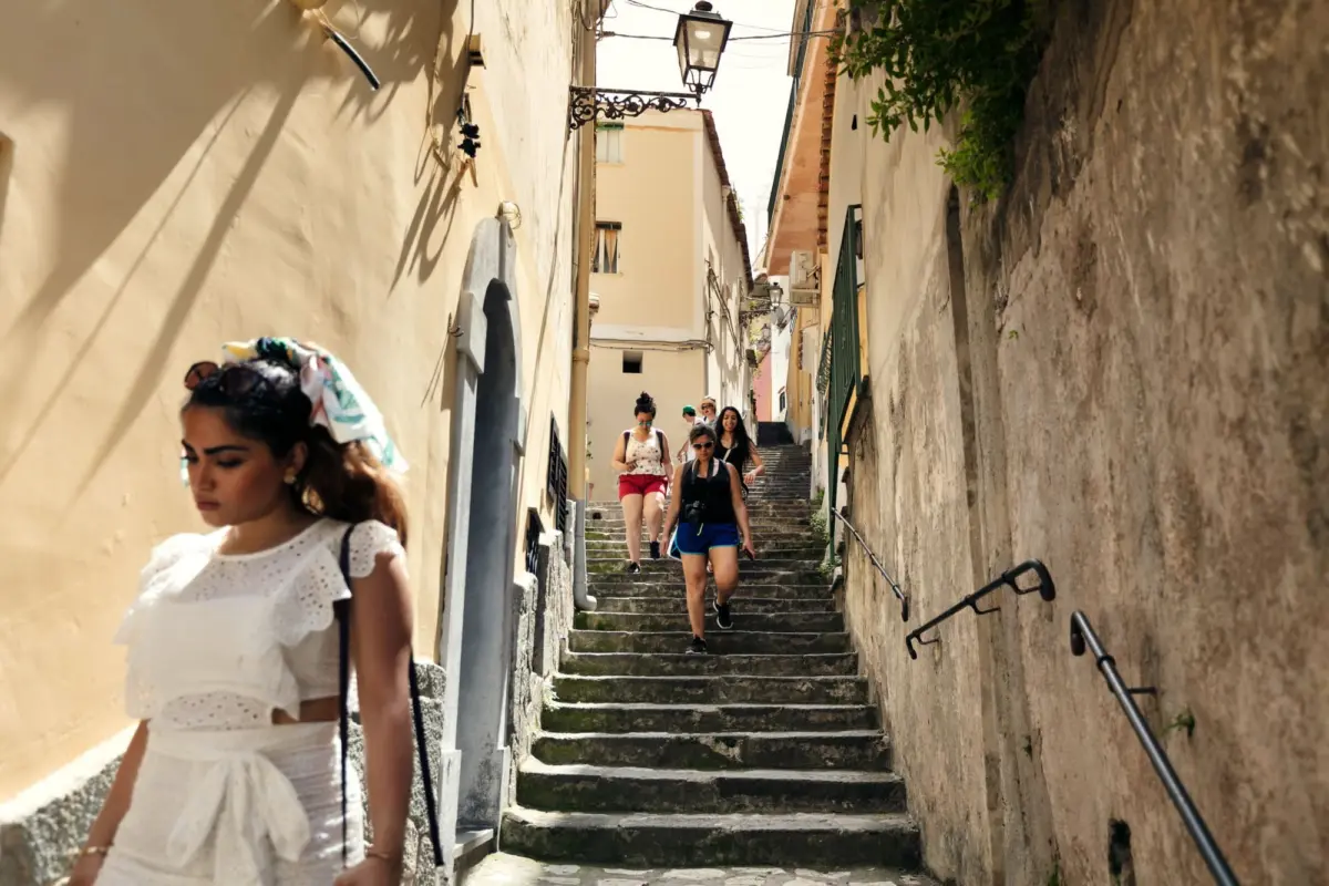 Group of women tourists walking down a sunlit narrow stone staircase in a historic alley.