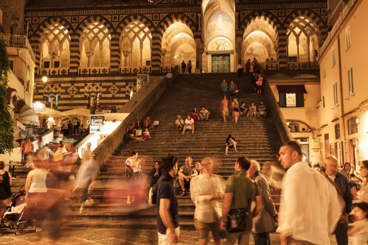 Spanish Steps at night in Rome, crowds moving on the stairway beneath striped arches and an illuminated facade.