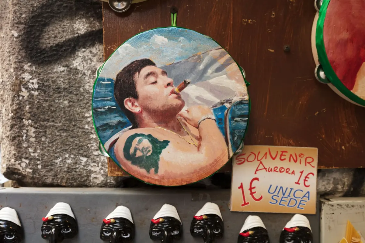 Round painted souvenir fan showing a person smoking a cigar, mounted on a wooden display beside other souvenirs.