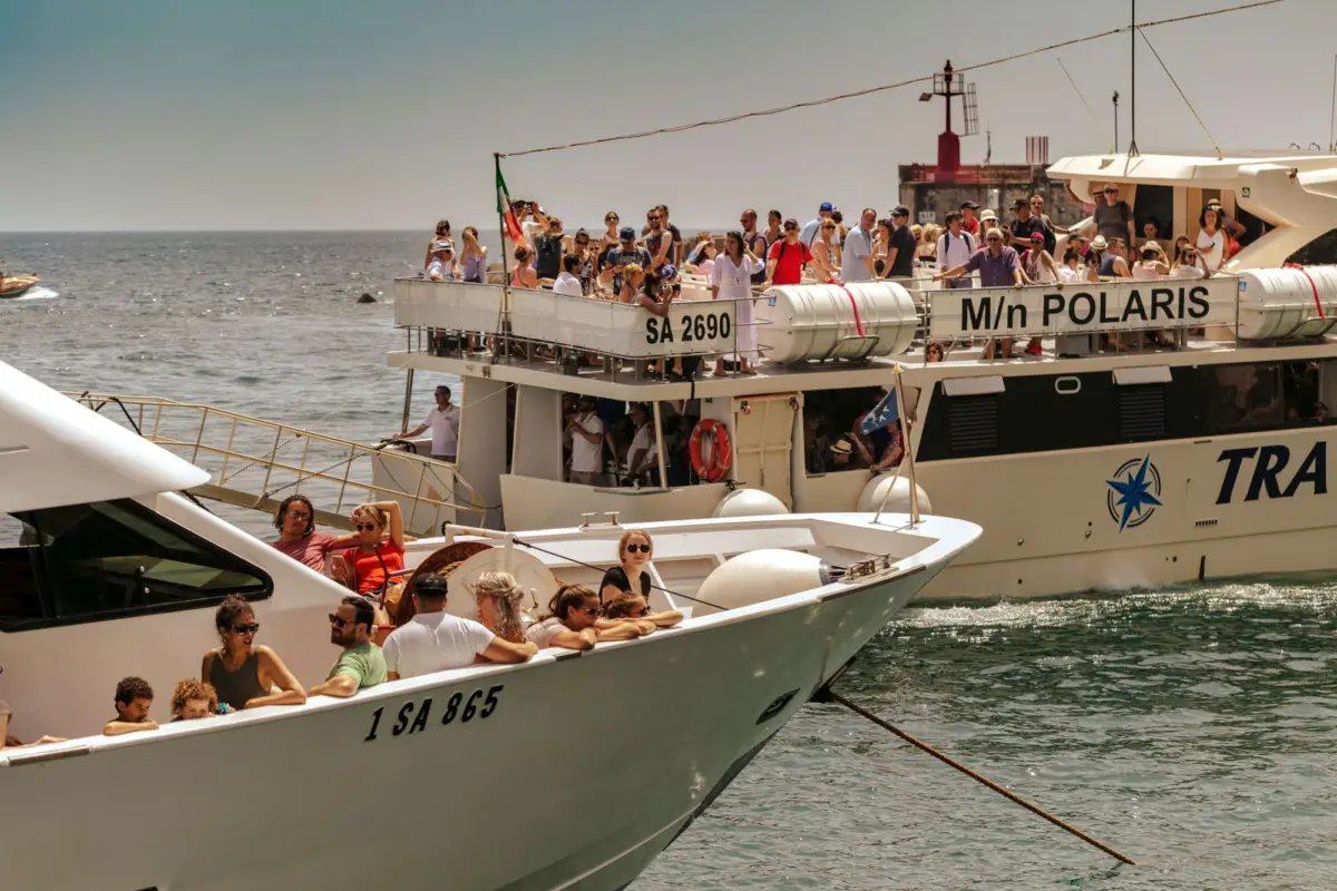 Crowded white tour boat, M/N POLARIS, with passengers on the upper deck near the harbor and a distant lighthouse.