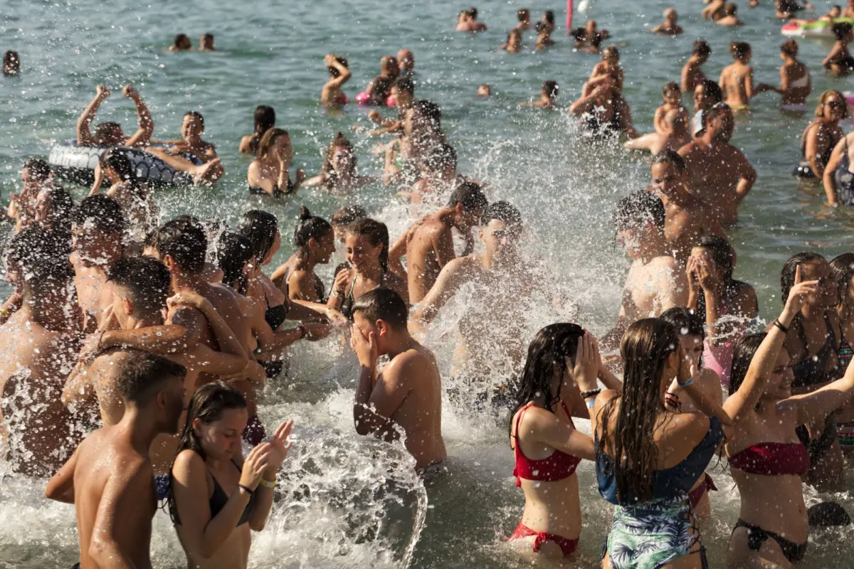 Crowded beach with numerous swimmers splashing in the surf along the shoreline.
