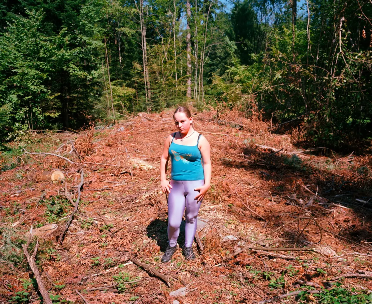 Person wearing turquoise tank top and lavender leggings stands in a sunlit forest clearing among fallen leaves and branches.