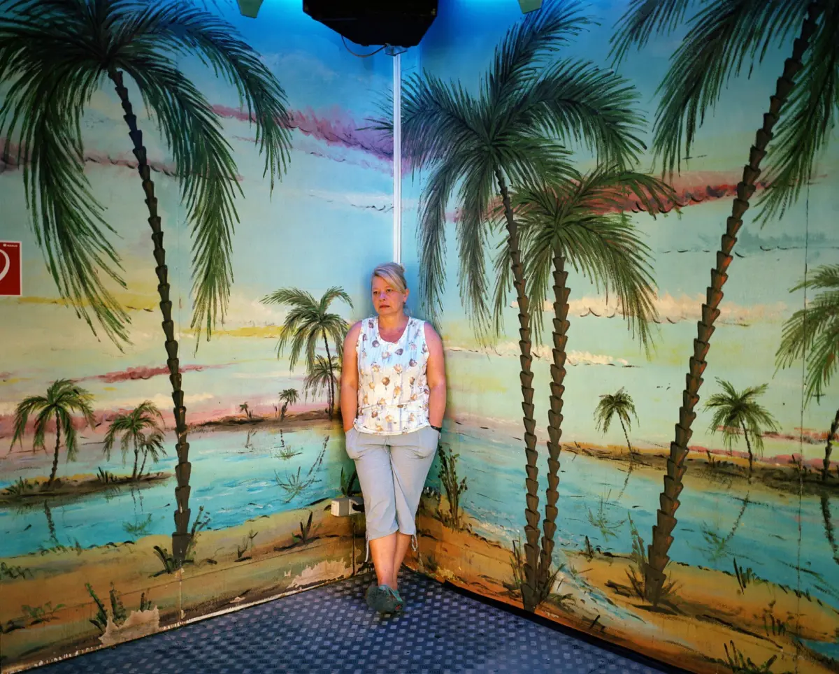 Adult person standing before a tropical beach mural featuring palm trees on a wall.